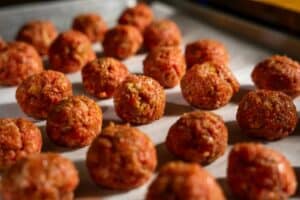 rolled, raw meatballs on a parchment-sheeted pan