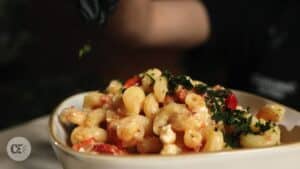 a bowl of baked feta pasta getting garnished with greens