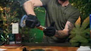A man in gloves vigorously shaking a bong filled with cleaning solution during a step-by-step guide on how to clean your bong.