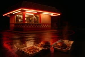 Late-night fast food scene with steaming burgers and fries outside a red checkerboard diner, representing stoner-friendly late-night cravings.