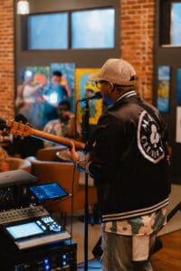 A musical performer with local art displayed in the background at Chronic Guru's artist showcase.