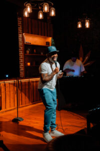 A comedian laughing while telling jokes on a Chronic Guru stage